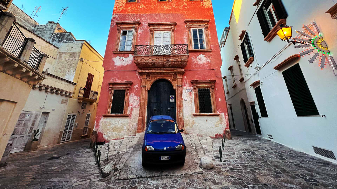 Fiat car in front of red house in Gallipoli, Italy.