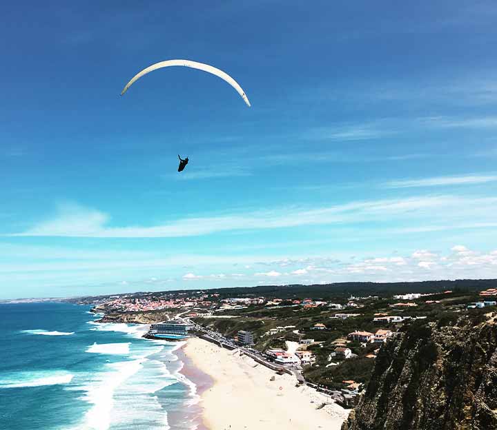 Paraglider flying over the beach in Cascais