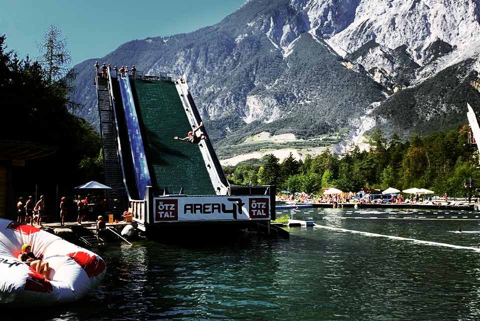 Person sliding off a freestyle ramp into an alpine lake