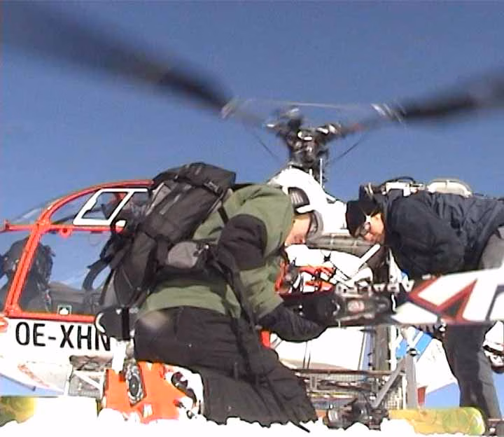 People crouching under helicopter blades on a snowy mountain
